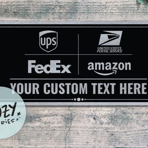 Op de afbeelding: Zwart rechthoekig bord met een zilveren rand. Het bord toont logo's van UPS, United States Postal Service, FedEx en Amazon. Daaronder staat de tekst "YOUR CUSTOM TEXT HERE". Een klein, rond logo voor "LITTLE COZY STORIES+" staat linksonder.