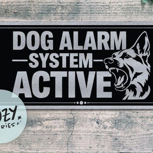 Può includere: Un cartello rettangolare nero e argento con le parole "DOG ALARM SYSTEM ACTIVE" e una grafica di un cane che ringhia. Il cartello è su uno sfondo grigio strutturato. Un piccolo logo rotondo per "Little Cozy Stories+" si trova nell'angolo in basso a sinistra.