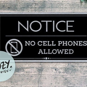 Puede incluir: Un letrero de metal negro y plateado con el texto "NOTICE" en letras grandes y "NO CELL PHONES ALLOWED" en letras más pequeñas. Un gráfico de un teléfono celular con una línea diagonal que lo atraviesa está por encima del texto.