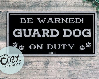 May include: Black and white sign with the text "BE WARNED! GUARD DOG ON DUTY" with paw prints on either side of the text.