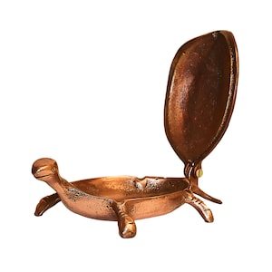 May include: A copper turtle-shaped ashtray with a hinged lid. The lid is open, revealing the interior of the ashtray.