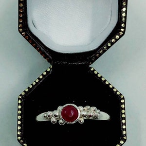 Puede incluir: Un anillo de plata con una piedra preciosa roja engastada en el centro. El anillo est&aacute; rodeado de peque&ntilde;as cuentas de plata.