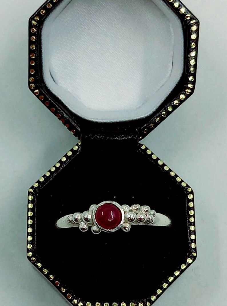 Puede incluir: Un anillo de plata con una piedra preciosa roja engastada en el centro. El anillo est&aacute; rodeado de peque&ntilde;as cuentas de plata.