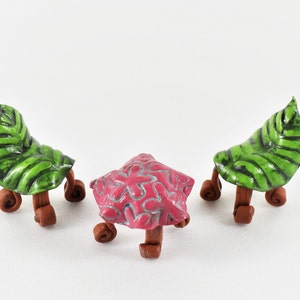 Puede incluir: Tres sillas en miniatura hechas de arcilla. Dos sillas son verdes con un diseño de hoja y cuatro patas marrones. La tercera silla es rosa con un diseño floral y cuatro patas marrones.