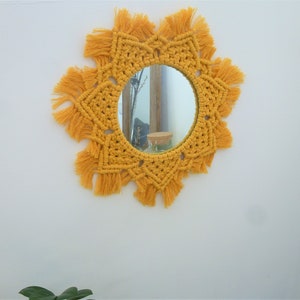 May include: A round mirror with a yellow macrame frame. The frame is made of knotted cords with fringe details.