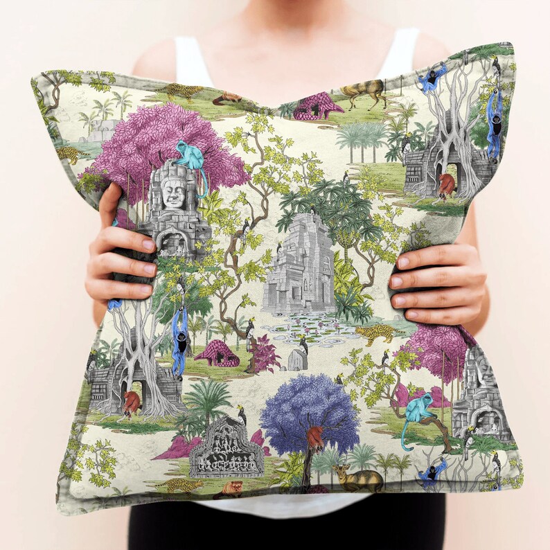 May include: A cream-coloured throw pillow with a colourful jungle scene featuring monkeys, temples, and lush foliage. The pillow has a pink, green, and blue colour scheme.
