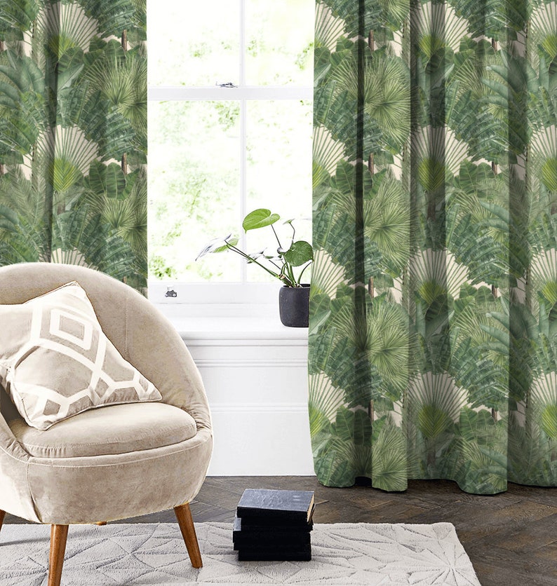 May include: A beige armchair with a white and beige patterned cushion sits in front of a window with green patterned curtains. The curtains feature a repeating pattern of large green leaves.