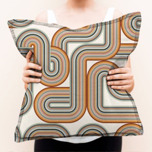 May include: A white cushion with a colourful geometric pattern of curved lines in shades of orange, yellow, blue, green, and brown. The pattern resembles a retro 70s design.