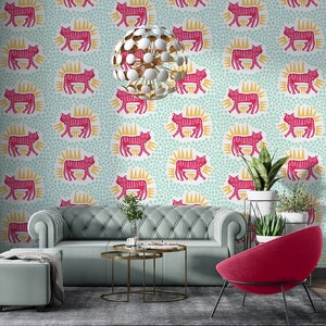 May include: A living room interior design featuring a teal blue sofa with a gold metal coffee table. The walls are covered in a wallpaper with a repeating pattern of pink tigers with yellow sunbursts on a light blue background. A pink chair and a potted plant are also visible.