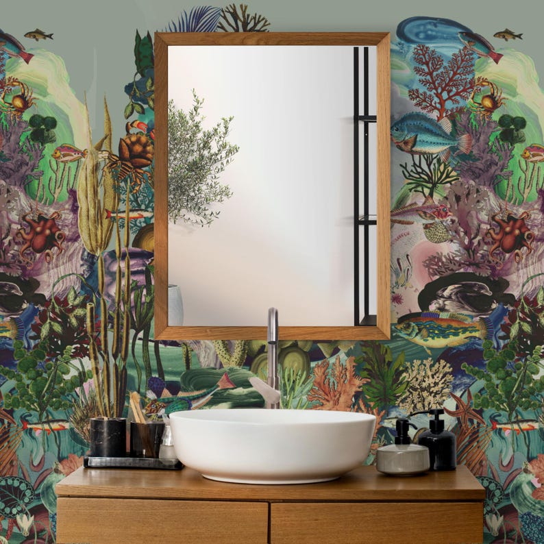May include: A bathroom vanity with a wooden cabinet, a white vessel sink, and a wooden-framed mirror. The wallpaper features a colourful underwater scene with fish, coral, and other marine life. Soap dispensers and a toothbrush holder are on the counter.