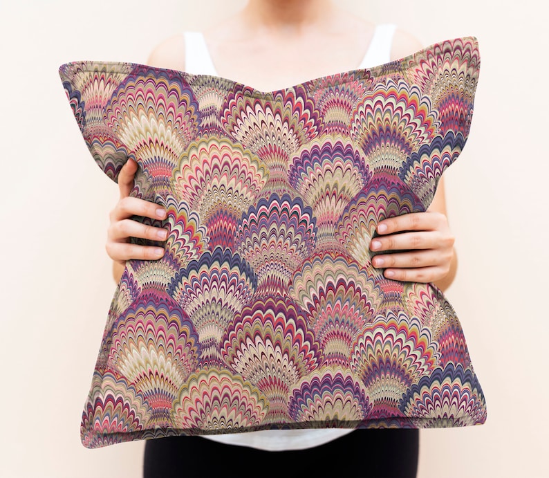 K&ouml;nnte beinhalten: Ein dekoratives Kissen mit einem farbenfrohen, abstrakten Muster aus &uuml;berlappenden Kreisen und Wirbeln in den Farben Lila, Rosa, Beige und Braun.
