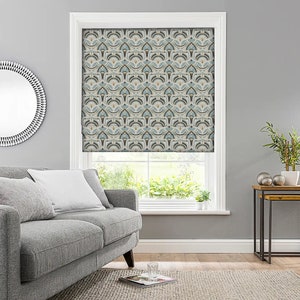 May include: A window with a patterned roller shade. The shade features a repeating geometric design in shades of blue, beige, and brown. The window is framed in white and the room has gray walls. A gray sofa and a round mirror are visible.