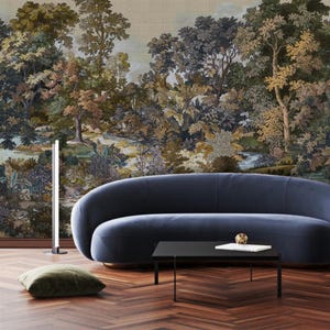 May include: A living room with a dark blue curved sofa, a black rectangular coffee table, and a floor lamp. The backdrop is a detailed mural depicting a forest landscape with trees, a river, and a muted colour palette.