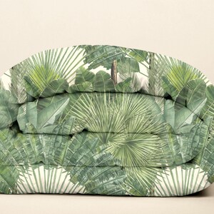 May include: A folded duvet cover with a tropical print featuring green palm leaves and banana leaves on a white background.