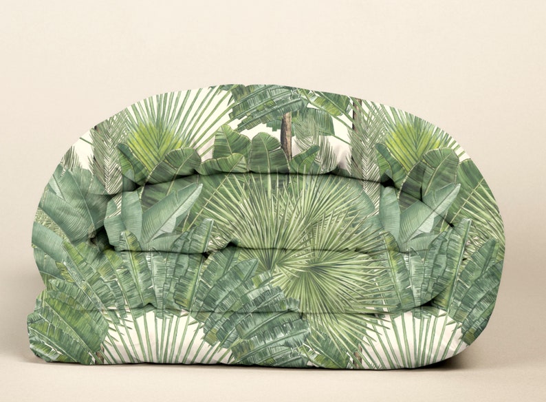 May include: A folded duvet cover with a tropical print featuring green palm leaves and banana leaves on a white background.