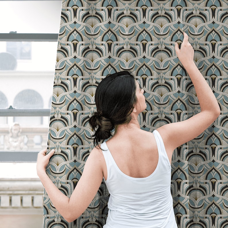 May include: A woman in a white tank top examines a patterned fabric. The fabric features a repeating Art Deco design in shades of blue, black, and gold. The pattern is a stylized fan shape.