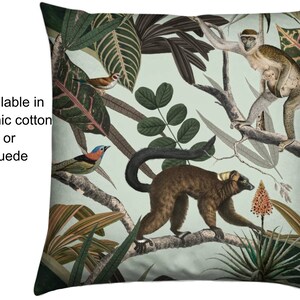 Könnte beinhalten: Quadratisches Kissen mit einem botanischen Design mit Affen, Vögeln und üppigem Laub in Grün-, Braun- und Blautönen. Das Kissen hat einen hellgrünen Hintergrund und den Text "Available in organic cotton or suede".