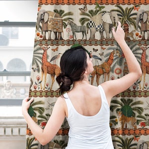 May include: A woman stands in front of a curtain featuring a colorful pattern of animals, plants, and geometric designs. The curtain has a cream background with orange, green, and blue accents. The animals include elephants, giraffes, zebras, and tigers.