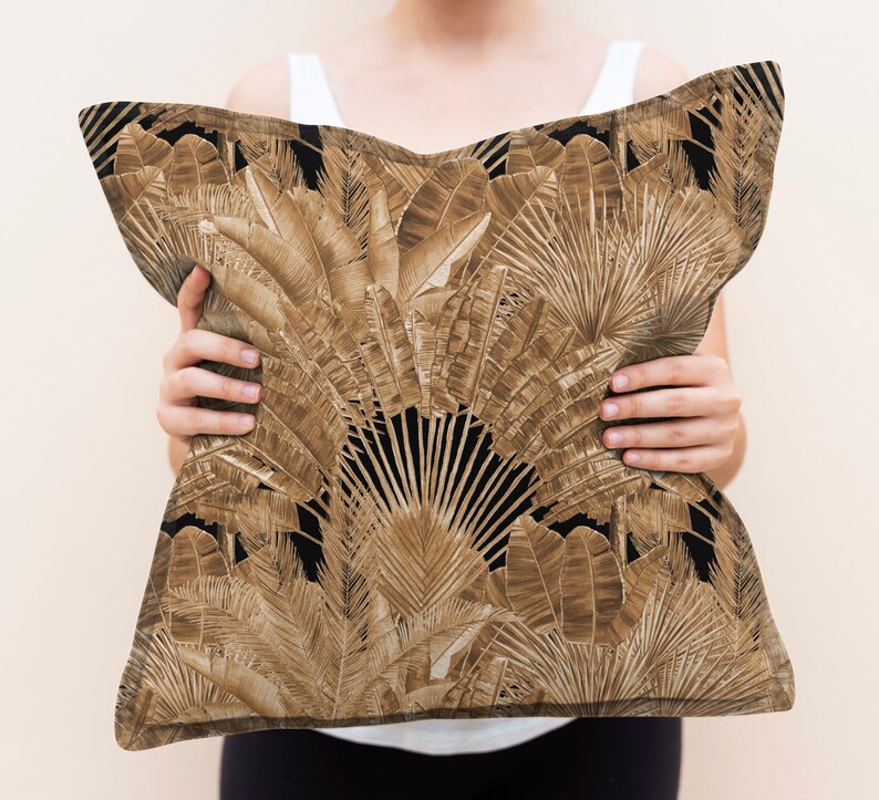 May include: A brown and black cushion with a tropical leaf pattern. The cushion is being held by a person.