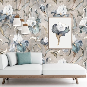 Puede incluir: Un sofá blanco con cojines azules se encuentra frente a una pared con un patrón de papel tapiz floral. El papel tapiz presenta iris blancos y azules con detalles dorados sobre un fondo gris.