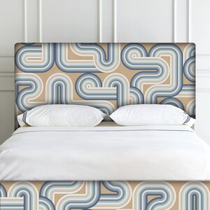 May include: A bed headboard featuring a geometric pattern of blue and beige curved lines. The headboard is made of fabric and has a modern design.