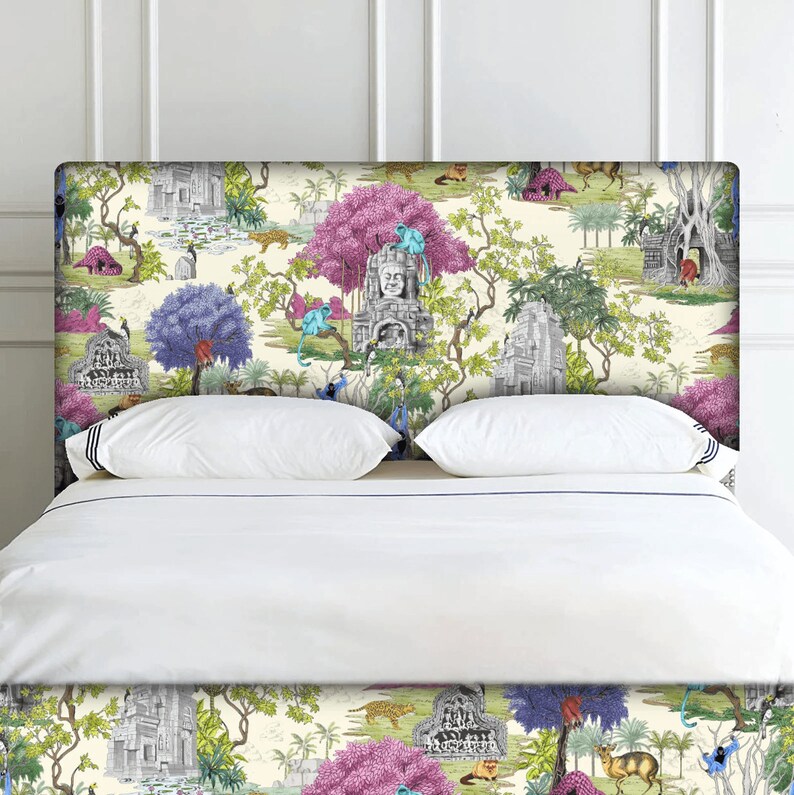 May include: A white bed with a patterned headboard featuring a jungle scene with pink trees, blue birds, and grey stone temples. The headboard is covered in a white fabric with a blue trim.