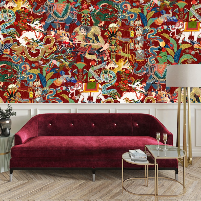 May include: A red velvet sofa with a gold metal frame sits in front of a wall with a colorful wallpaper featuring dragons, elephants, and other mythical creatures. A gold metal side table with two tiers sits in front of the sofa.