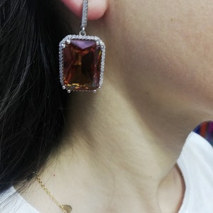 May include: A pair of dangle earrings featuring a large, rectangular, orange gemstone set within a border of small, clear gemstones.