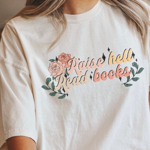 May include: A white t-shirt with a floral design and the text "Raise hell Read books" in a retro font.