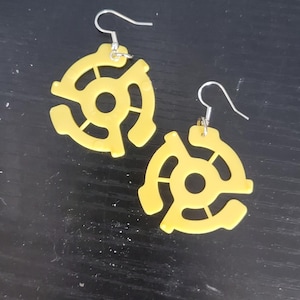 May include: A pair of yellow earrings shaped like a record adapter. The earrings have a silver hook.