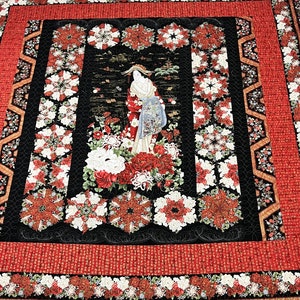 May include: A black and red quilt with a floral design featuring a woman in a traditional Japanese kimono. The quilt is made with a variety of fabrics and textures, and it has a beautiful, intricate design.