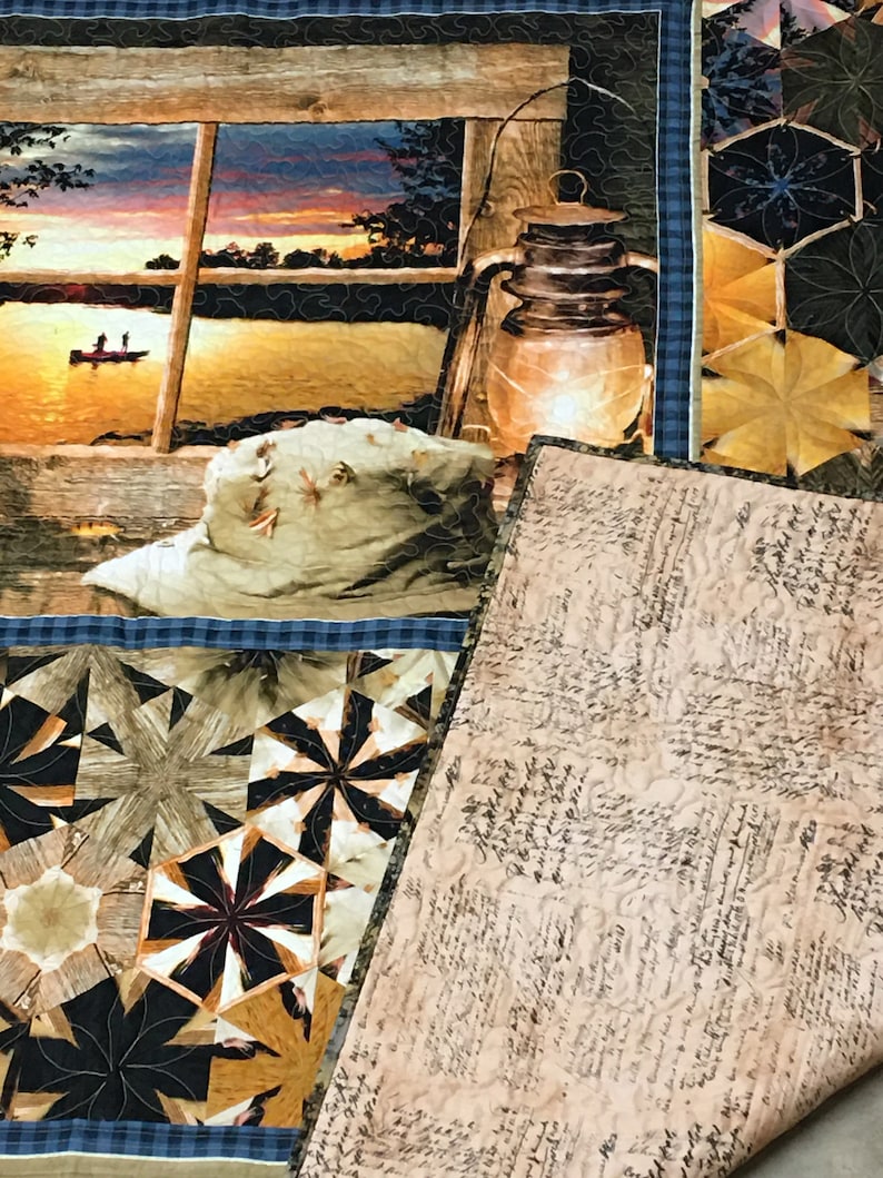May include: A quilt with a patchwork design featuring a variety of geometric shapes in shades of brown, black, and gold. The quilt is folded in half, revealing a beige fabric with a handwritten script pattern.
