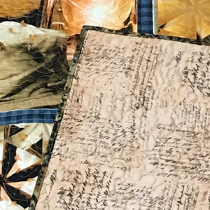 May include: A close-up of a beige fabric with a pattern of black handwritten script. The fabric is part of a quilt with other fabric squares visible in the background.