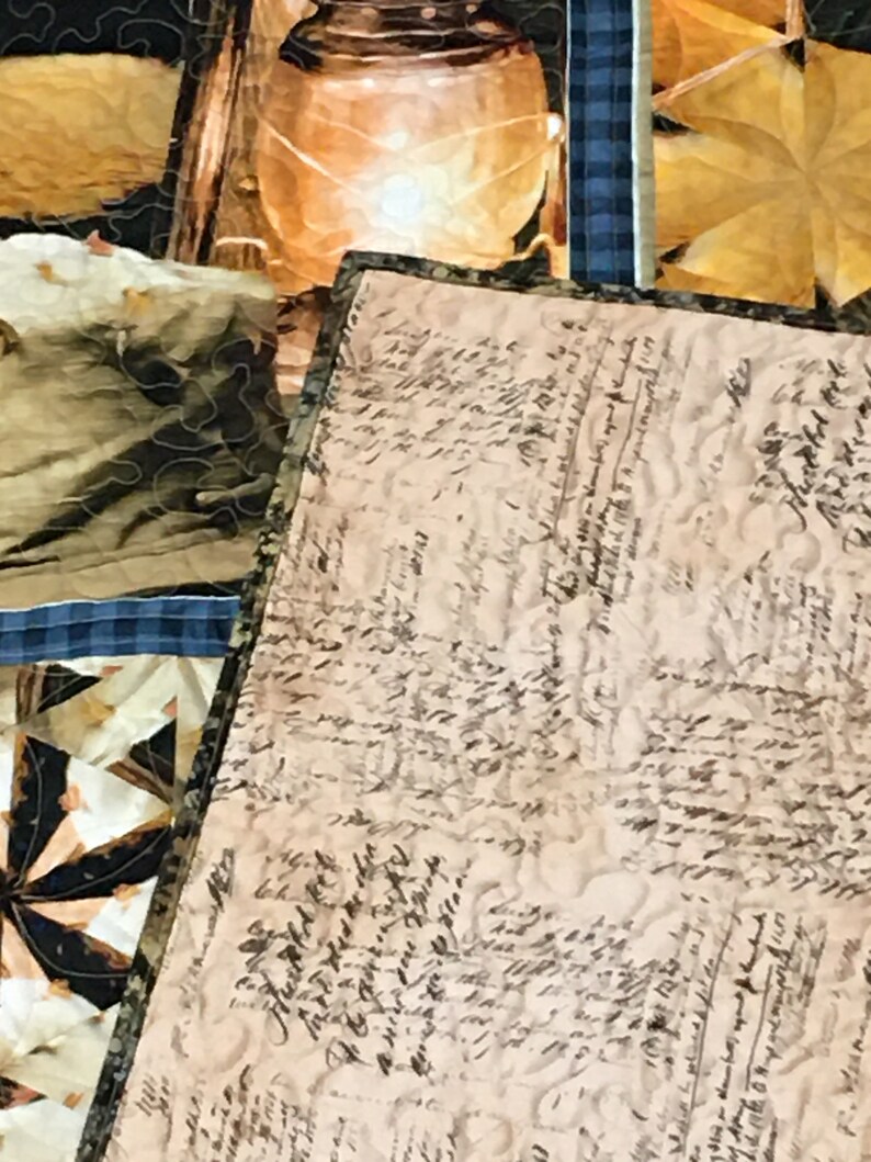 May include: A close-up of a beige fabric with a pattern of black handwritten script. The fabric is part of a quilt with other fabric squares visible in the background.
