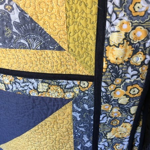 May include: A quilt with a patchwork design featuring yellow and grey fabric. The quilt is quilted with a free-motion quilting design. The quilt is edged with black fabric.