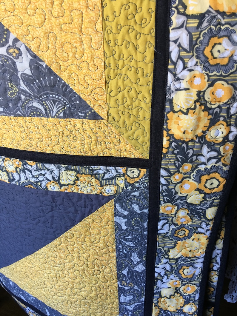 May include: A quilt with a patchwork design featuring yellow and grey fabric. The quilt is quilted with a free-motion quilting design. The quilt is edged with black fabric.