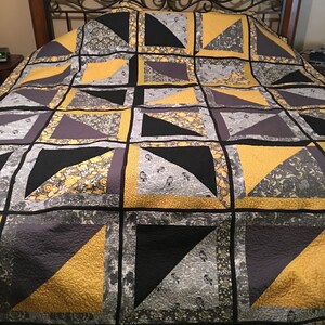May include: A quilt with a geometric pattern in shades of black, grey, and yellow. The quilt is made of squares and triangles, and it has a floral border.