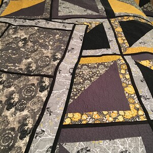 May include: A quilt with a patchwork design featuring black, grey, and yellow fabric. The quilt is made up of squares and triangles, and the fabric has a variety of patterns, including floral, geometric, and abstract.