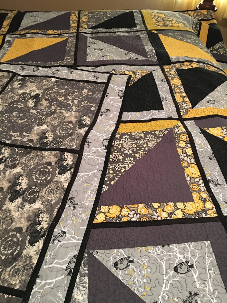 May include: A quilt with a patchwork design featuring black, grey, and yellow fabric. The quilt is made up of squares and triangles, and the fabric has a variety of patterns, including floral, geometric, and abstract.