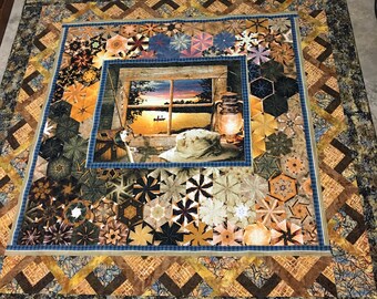 May include: A quilt with a patchwork design featuring a variety of geometric shapes in shades of brown, blue, and beige. The center of the quilt features a window scene with a lake and a boat in the distance.