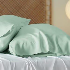 May include: Two light green pillowcases made of soft, smooth fabric. The pillowcases are lying on a white bed sheet.