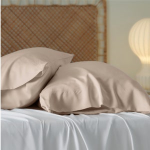 May include: Two light brown pillowcases on a white bed. The pillowcases are made of a soft, smooth fabric.