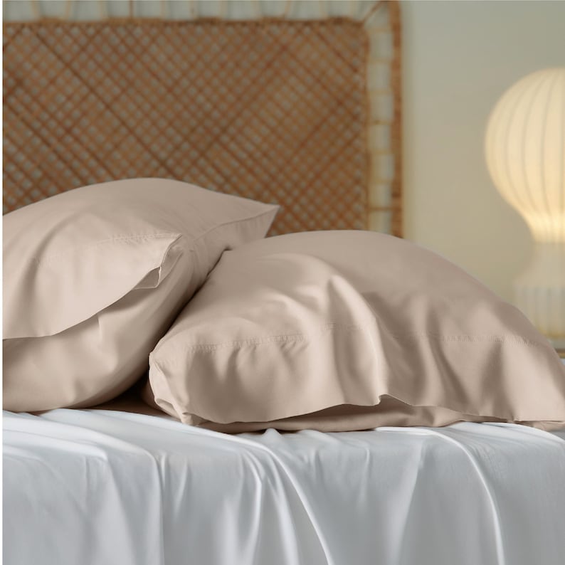 May include: Two light brown pillowcases on a white bed. The pillowcases are made of a soft, smooth fabric.