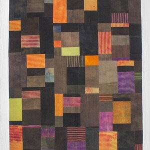 Può includere: Un quilt patchwork con una varietà di colori e motivi, tra cui arancione, viola, marrone e nero. Il quilt è composto da quadrati e rettangoli di diverse dimensioni.