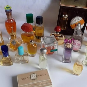 Può includere: Una collezione di flaconi di profumo in miniatura di vari colori e forme, tra cui vetro trasparente, vetro ambrato e vetro smerigliato. Alcuni flaconi hanno tappi decorativi, come un tappo verde a forma di gemma e un tappo dorato. I flaconi sono disposti su una superficie, con alcuni flaconi in primo piano e altri sullo sfondo.