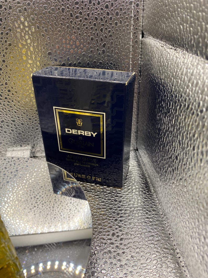 May include: A navy blue box of Derby by Guerlain aftershave. The box has gold lettering and a gold border. The text on the box reads "AFTER SHAVE lotion apr&egrave;s rasage, parfum&eacute;e" and "1.7 fl. oz. N&deg; 762".