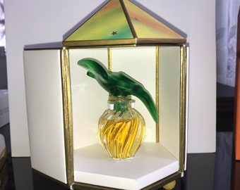 Può includere: Un flacone di profumo in vetro giallo con un tappo a forma di foglia verde all'interno di una teca bianca e dorata con un coperchio colorato a forma di stella.