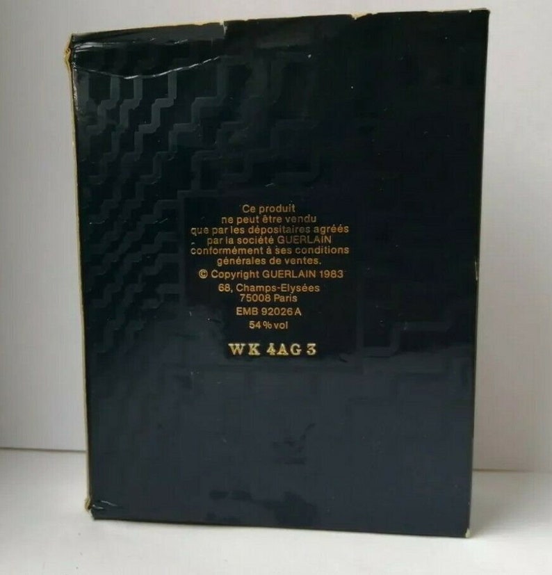 May include: A black box with gold geometric patterns and white text. The text includes "Copyright GUERLAIN 1983" and "54% vol". The box has a slightly worn appearance.