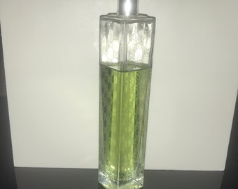 May include: A rectangular perfume bottle with a silver cap. The clear glass bottle is filled with a light green liquid and is etched with a repeating pattern. The bottle is approximately 6 inches tall.