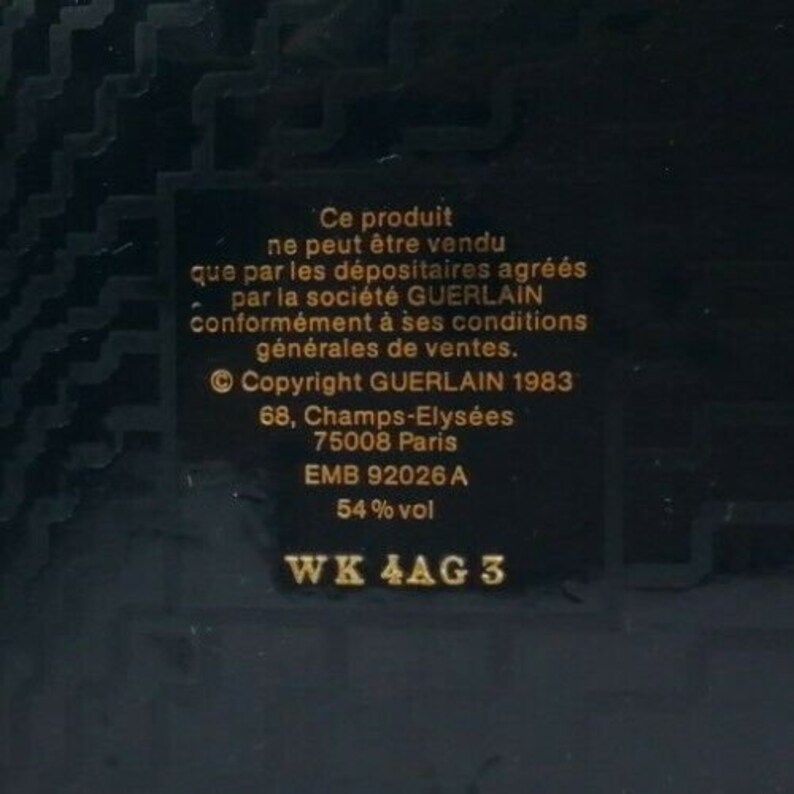 May include: A dark background with a rectangular label featuring gold text. The text includes the phrase "Ce produit ne peut &ecirc;tre vendu" and "Copyright GUERLAIN 1983". Additional text includes the address "68, Champs-Elys&eacute;es, 75008 Paris" and "54% vol".